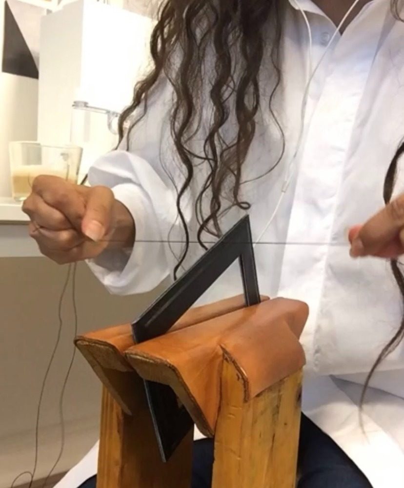 The maker saddle-stitching a leather piece by hand on a wooden stitching pony