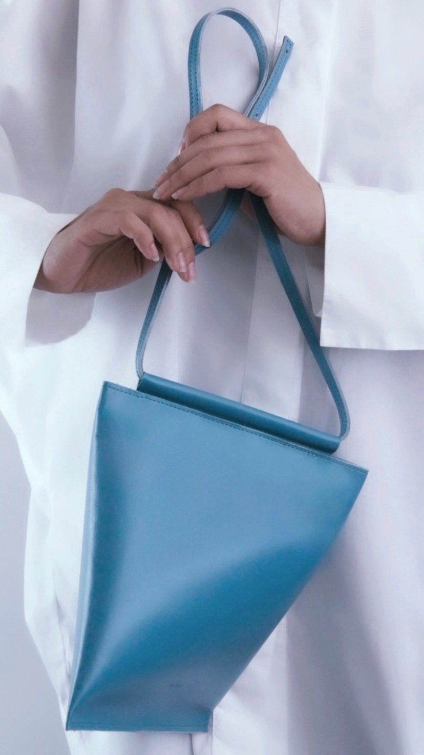 An Angular Momentum bag in teal-blue leather, held by its strap to show its rotated silhouette