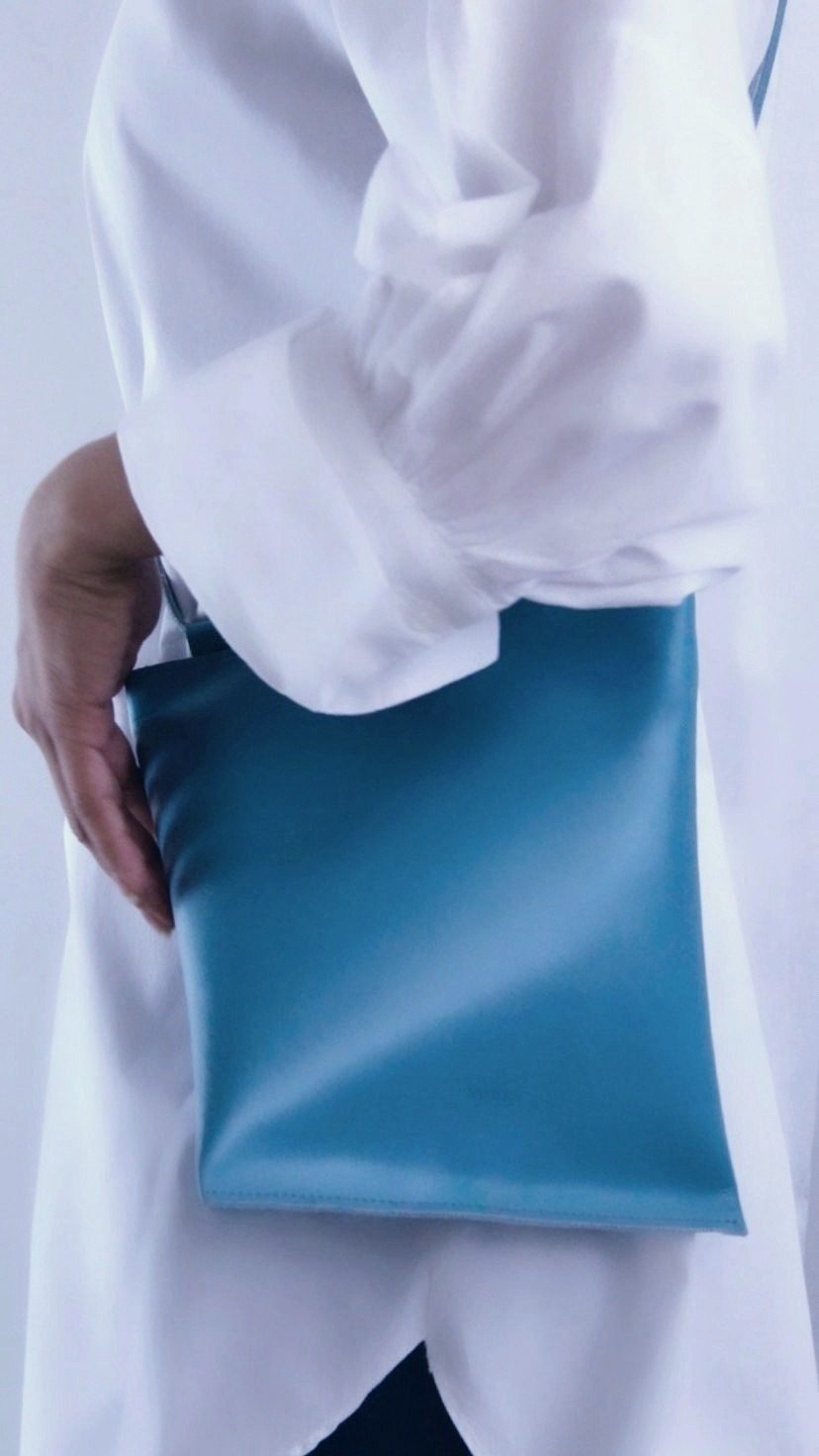 Angular Momentum, a teal-blue leather bag carried flat under the arm