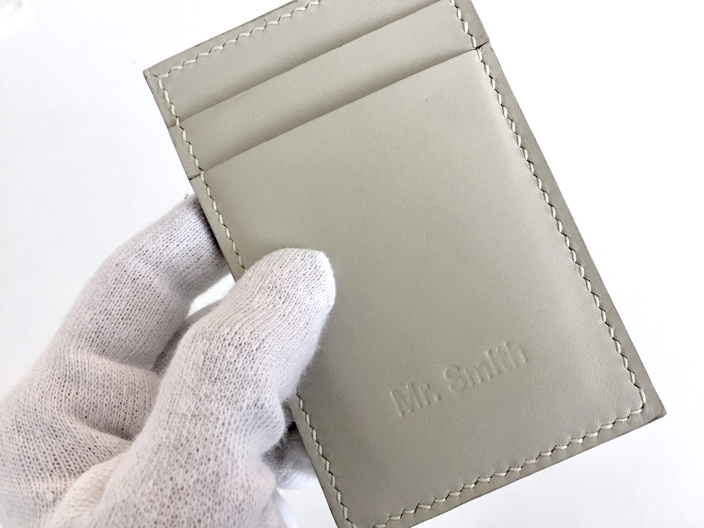 A gloved hand holding a bone leather card holder embossed with a customer name