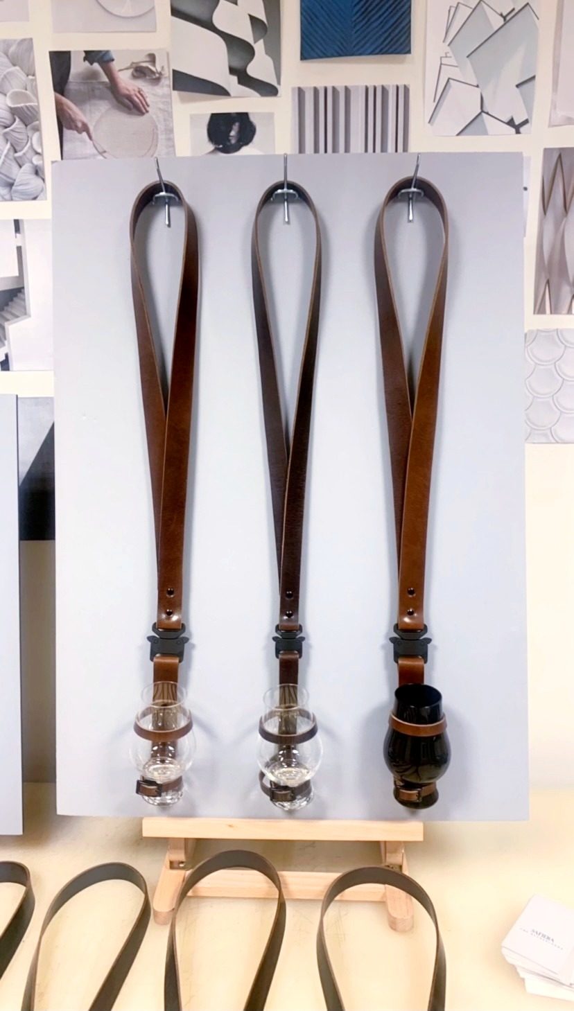 Three hand-stitched leather whisky cords hung on a studio wall, each cradling a tasting glass