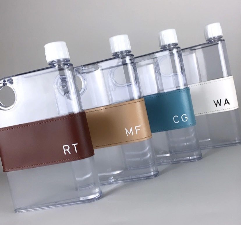 Four flat Safiera water bottles, each in a leather sleeve embossed with different initials