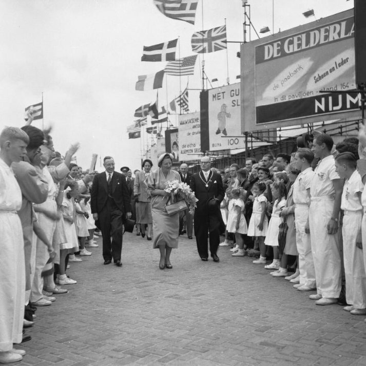 Queen Juliana walking between rows of well-wishers and flags at an international leather exhibition in 1953